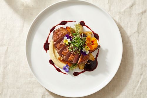 Placeholder stock photo: a seared duck breast plated with a purée, roasted vegetables, and edible flowers.